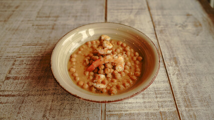 Fototapeta na wymiar Chickpea stew with spanish prawns on wooden table in a restaurant