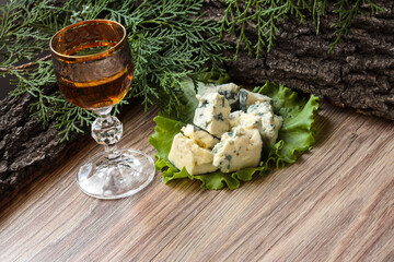 Cheese cubes on a lettuce leaf with a stack of cognac on the background of tree bark.