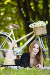 Fototapeta premium Blond girl sitting near her bike in summer park