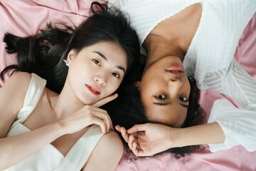 Obraz na płótnie Canvas Asian and african women in white shirt laying on pink cloth.