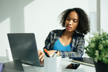 African woman working in office with laptop and smartphone.