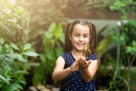 Little girl holding butterfly in her hand.