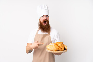 Redhead man in chef uniform. Male baker holding a table with several breads with surprise facial expression