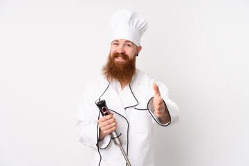 Redhead man using hand blender over isolated white background handshaking after good deal