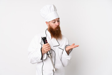 Redhead man using hand blender over isolated white background holding copyspace imaginary on the palm