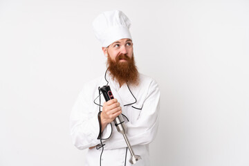 Redhead man using hand blender over isolated white background thinking an idea