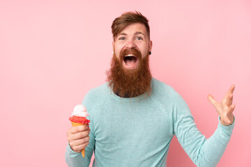 Redhead man with long beard holding a cornet ice cream over isolated pink background with shocked...