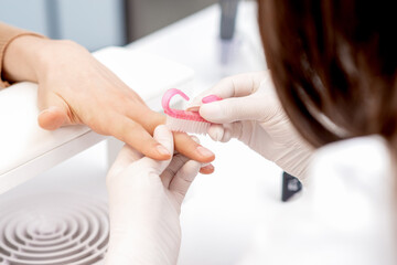 Close up of manicure master in white gloves uses brush to clean dust from female nails in beauty salon