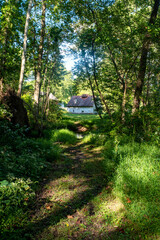 Picturesque scene of a white stone cabin with red roof at the end of a woodland hiking trail.