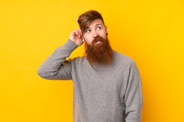 Redhead man with long beard over isolated yellow background having doubts
