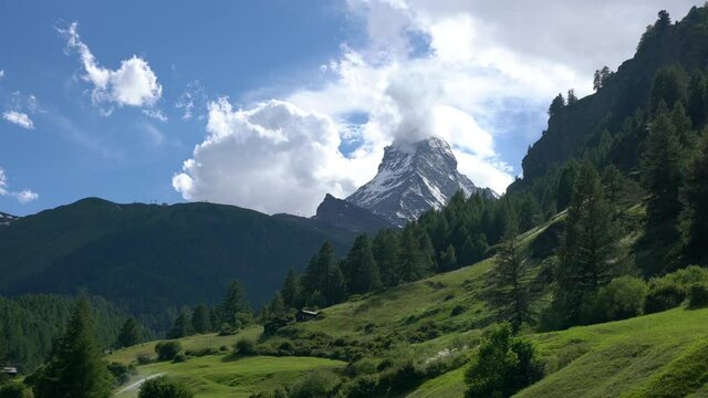 Timelapse of the Matterhorn mountain summit with snow clouds blue sky and green nature during summer in Zermatt Switzerland