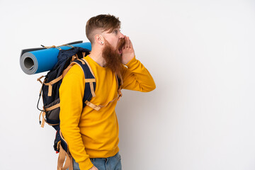 Young mountaineer man with a big backpack over isolated white background shouting with mouth wide open