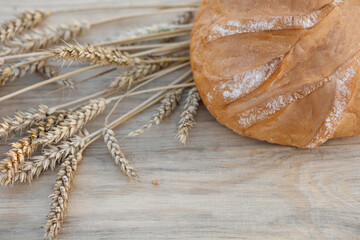 round bread and ears of wheat lie on a light wooden table (top view)