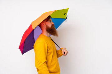 Redhead man with long beard holding an umbrella over isolated white background looking side