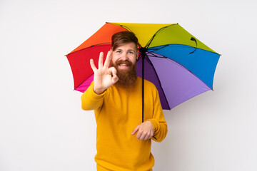 Redhead man with long beard holding an umbrella over isolated white background showing an ok sign with fingers