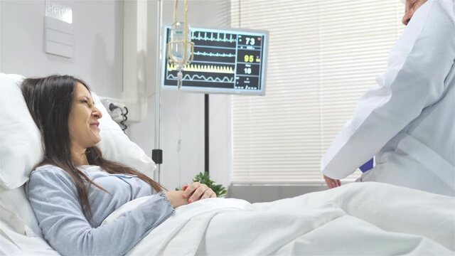 caring doctor visits mature woman on hospital bed,friendly doctor holding patient hand and talking to her,positive feeling good news
