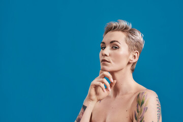 Beauty portrait of a young attractive half naked tattooed woman with perfect skin looking...