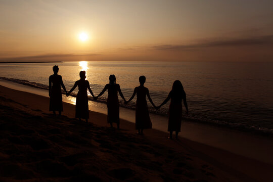 cinco mujeres cogidas de la mano al amanecer en la playa