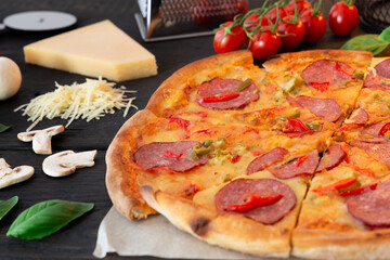 Tasty hot pizza with ingredients and pizza cutting knife on a black texture background. Top view
