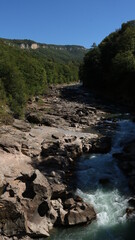 a clear, rough mountain river seethes among large rough stones against the backdrop of a beautiful landscape of a plateau and a bright blue sky