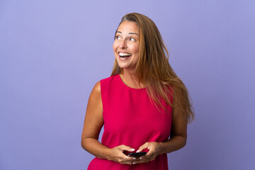 Middle age brazilian woman isolated on purple background using mobile phone and looking up