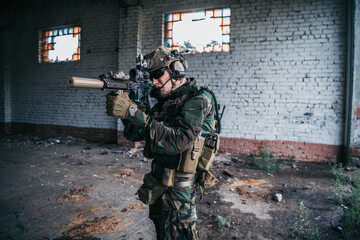 Fototapeta premium Military man with assault rifle standing inside building, he is ready for combat