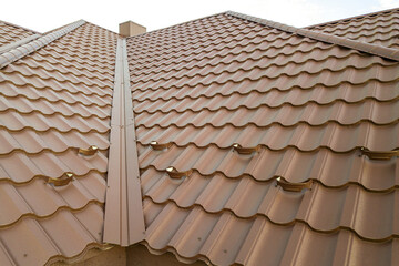 Detail of a house roof surface covered with brown metal tile sheets.
