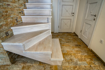 Stylish wooden contemporary staircase inside loft house interior. Modern hallway with decorative limestone brick walls and white oak stairs.