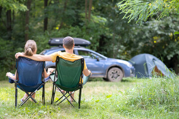 Happy couple sitting on chairs at campsite hugging together. Travel, camping and vacations concept.