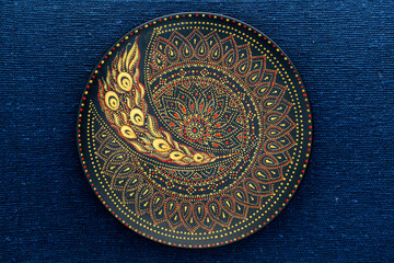 Decorative ceramic plate with black, red and golden colors, painted plate on the background of blue fabric, dot painting