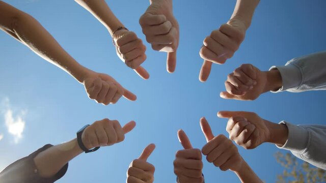 Bottom view of young people standing in a circle and showing thumbs up