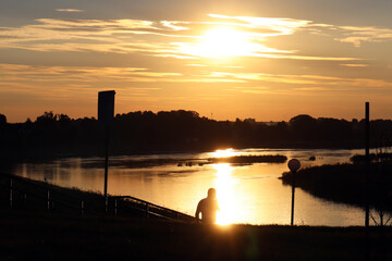 Fototapeta premium Beautiful sunset landscape on the river. Silhouette of a man on a background of water. Vacation and travel concept.
