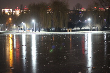 Lights of the night city and a frozen lake in a night city park