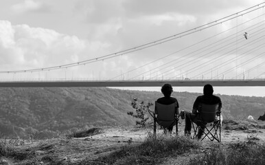 Two people sitting against the Yavuz Sultan Selim Bridge

