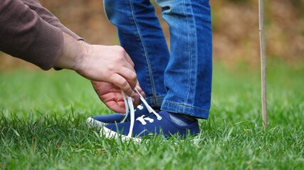 Detail of parent hands tie child laces in nature, helpful parental role, conceptual, first ability