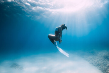 Freediver glides over sandy sea with white fins. Attractive woman free diver in blue ocean