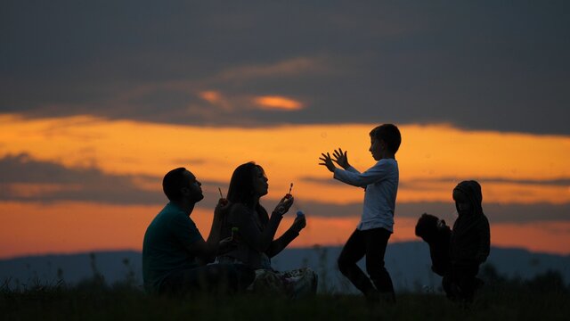 Young parents silhouettes blowing bubbles and happy children play, red sunset sky in background - Powered by Adobe