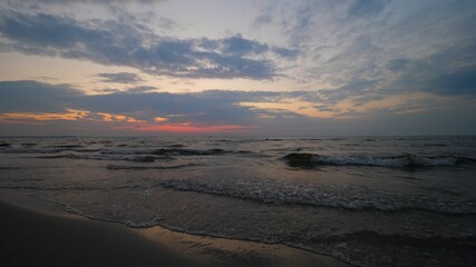 Sea waves on sandy beach, sunset clouds on colorful sky