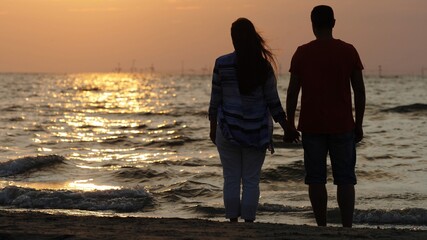Couple of lovers silhouettes  holding hands standing at seashore, admire sunrise