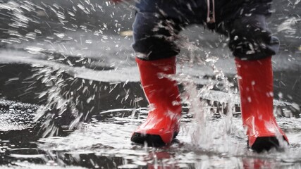 Detail of child rubber red boots jumping on rain puddle