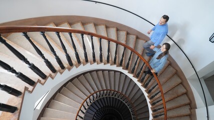 Lovers couple just married stepping up the spiral stairs of modern house with its elegant...
