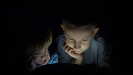 portrait of brothers look at tablet screen in dark, children under blanket, technology