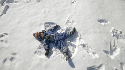 Funny child lies on ground and makes snow angel, up view, enjoy winter
