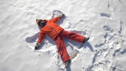 Fototapeta na wymiar One child lies on ground and makes snow angel, winter fun