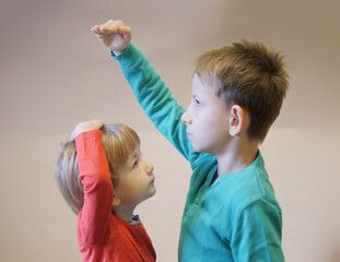 Happy children measuring to determine who is bigger, power struggle, funny youngest brother...
