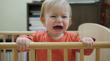 Portrait on sad child cry and scream in little baby crib, desire to reach out, lonely kid