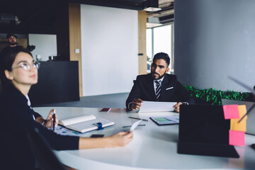 Turkish male employee formally dressed sitting at desktop and listening business information during briefing collaboration in office, Hispanic proud ceo have productive brainstorming with colleagues