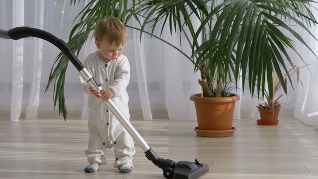 Amusing baby child look curious at vacuum cleaner willing to teach to use it