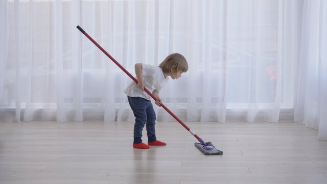 Smart funny child with mop cleaning careful floor using finger, meticulous work