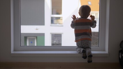 Little baby child on his knee look outside on window, waiting to go outdoor